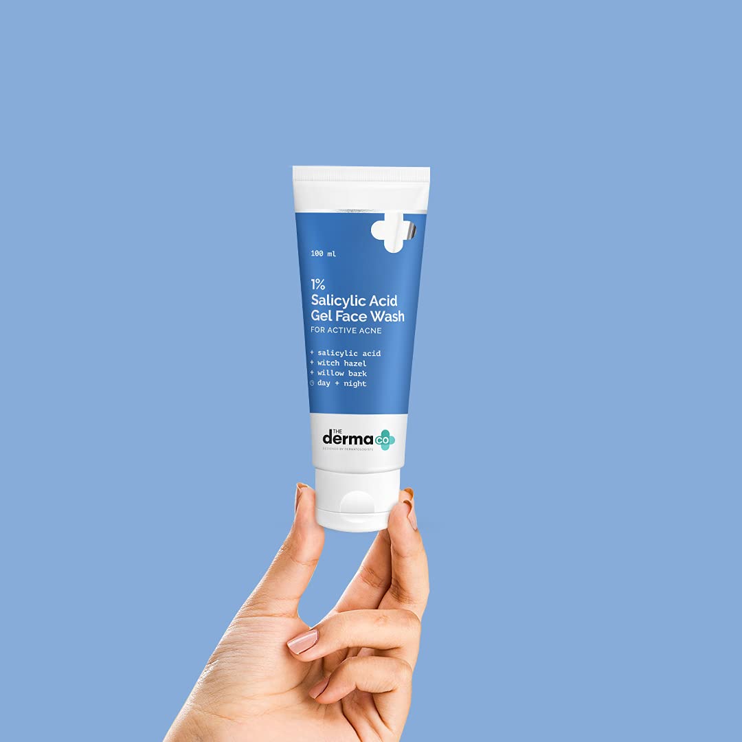 Hand holding a tube of derma e Salicylic Acid Gel Face Wash against a blue background