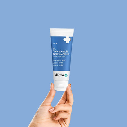 Hand holding a tube of derma e Salicylic Acid Gel Face Wash against a blue background