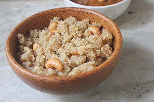 Wooden bowl filled with a grain-based dish topped with nuts on a light surface.
