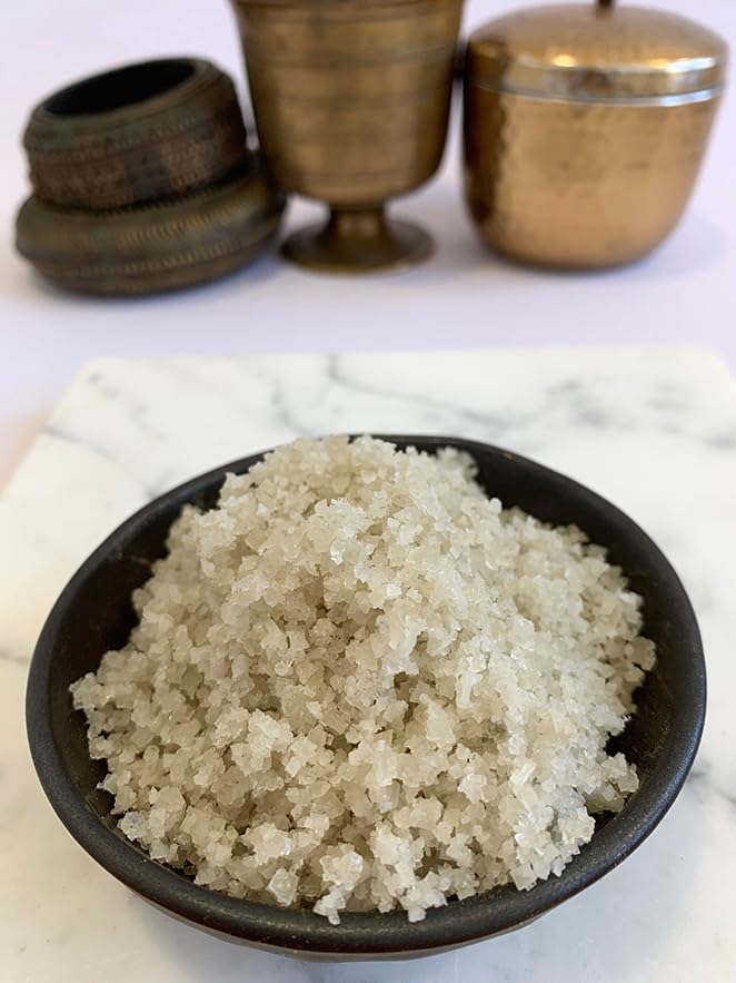 Small bowl of white granulated product on a marble surface with bronze containers in the background.