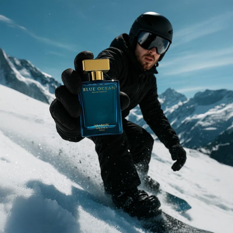 Person snowboarding holding a Blue Ocean perfume bottle with mountains in the background