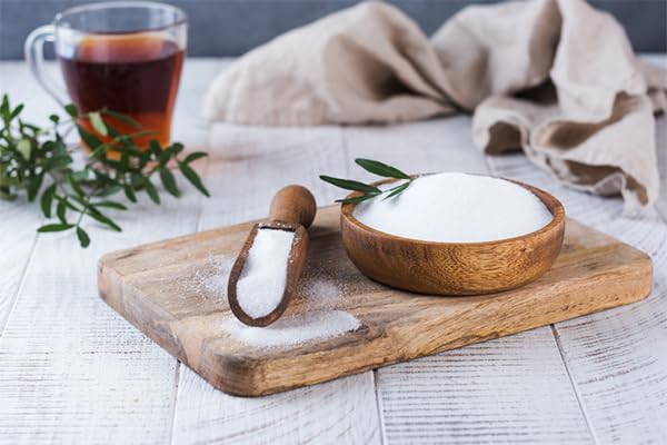 Wooden bowl with salt, wooden scoop, and a cup of tea on a wooden board.