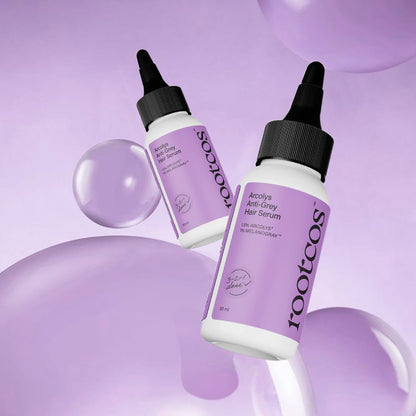 Two bottles of rootcos Acetyle Anti-Grey Hair Serum on a purple background with bubbles.