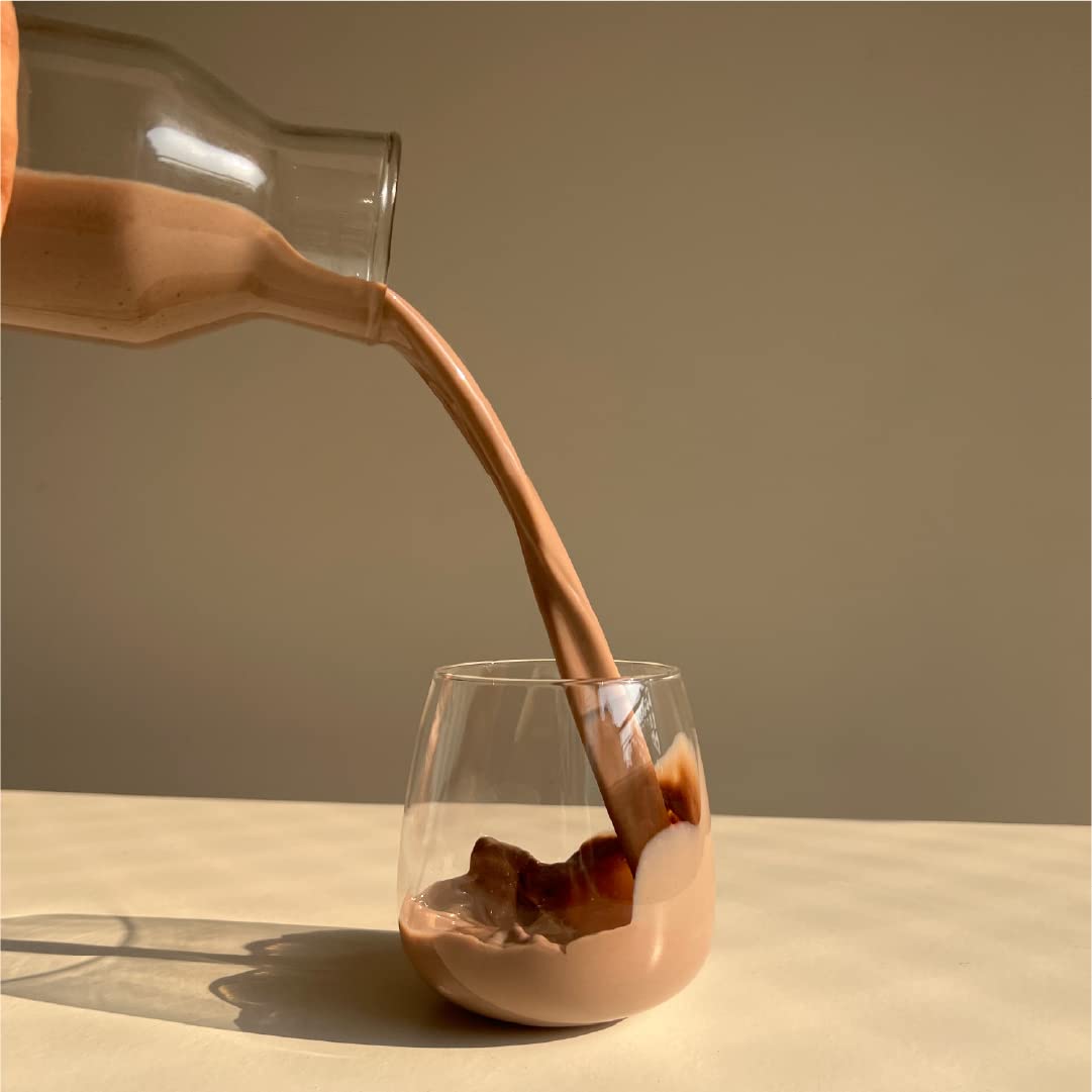 Chocolate milk being poured from a bottle into a glass on a neutral background