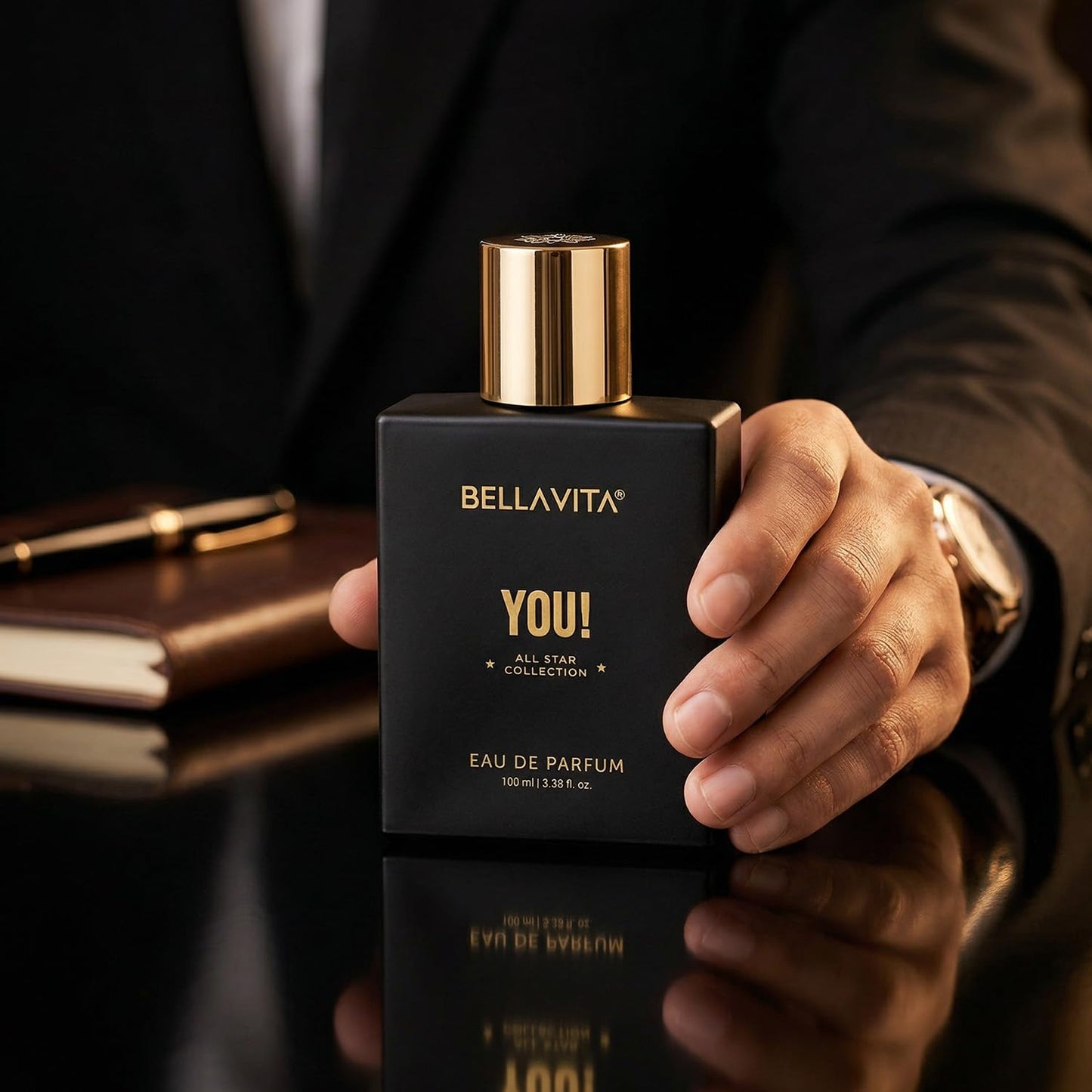 Hand holding a black Bellavita perfume bottle with gold cap on a reflective surface.