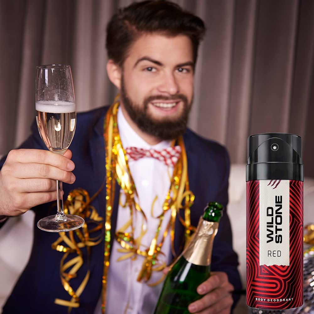 Man in festive attire holding a glass of champagne and a bottle, with a Wild Stone Red deodorant can in the foreground.