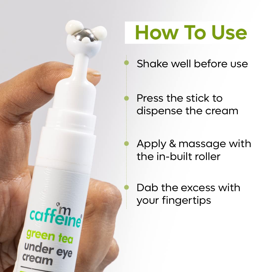Hand holding a white under eye cream with usage instructions on a light gray background