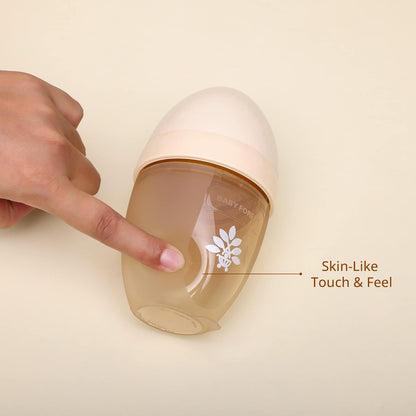 Hand touching a baby bottle with 'Skin-Like Touch & Feel' text on a beige background