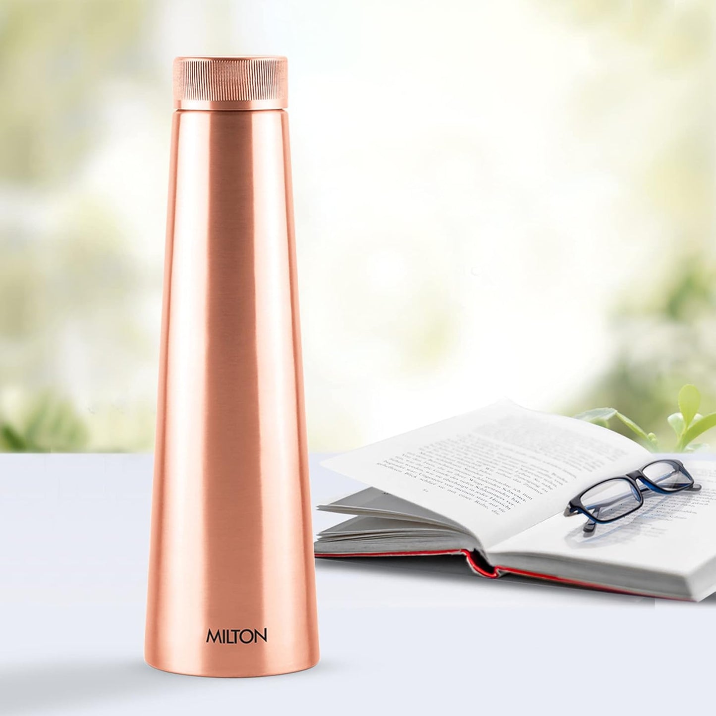 Rose gold Milton water bottle on a table with an open book and glasses