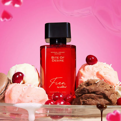 Red perfume bottle labeled 'Bite of Desire' surrounded by ice cream and cookies on a pink background