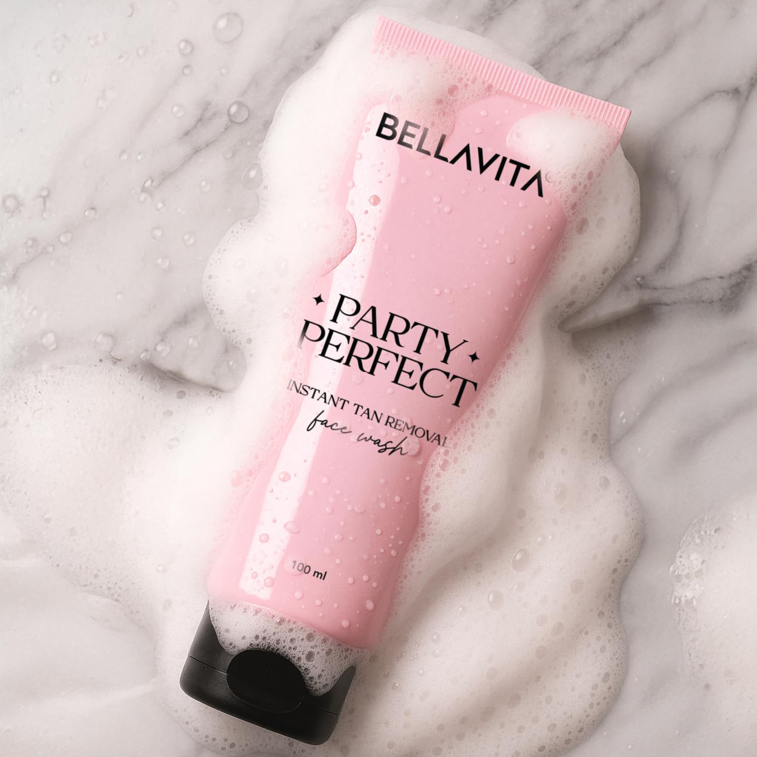 Pink tube of Bellavita Party Perfect face wash on a marble surface with foam.