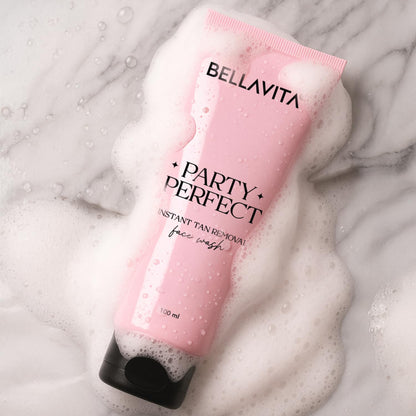 Pink tube of Bellavita Party Perfect face wash on a marble surface with foam.