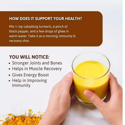Glass of yellow liquid held by hands with turmeric powder on a white background