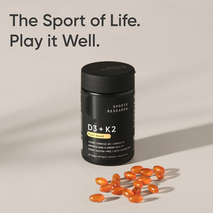 Black supplement bottle labeled 'D3 + K2' with orange capsules on a beige background, featuring the text 'The Sport of Life. Play it Well.
