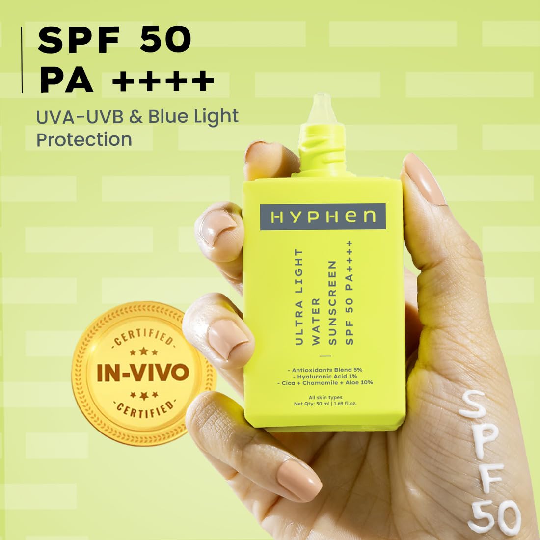 Hand holding a yellow HYPHEN sunscreen bottle with SPF 50 on a green background