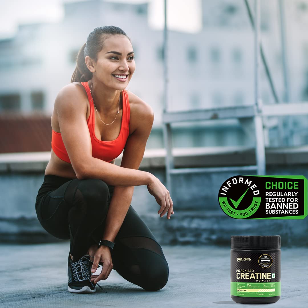 Woman in athletic wear squatting outdoors with Optimum Nutrition creatine supplement in the foreground.