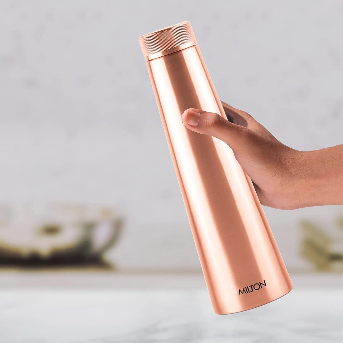 Rose gold thermos held by a hand with a blurred background