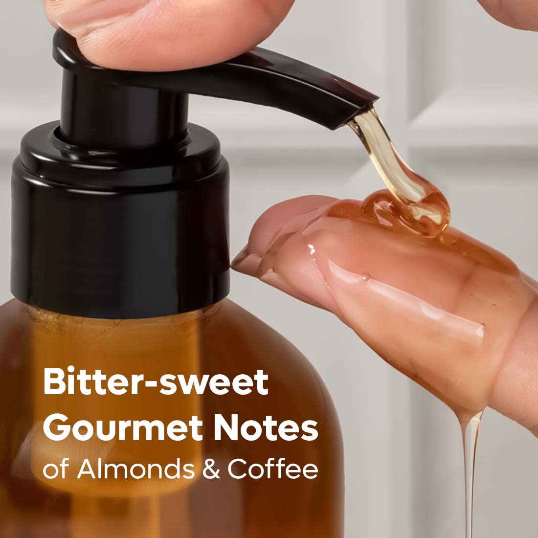 Bottle of almond coffee with a pump being pressed, showing a hand holding the pump and a small amount of liquid dripping.