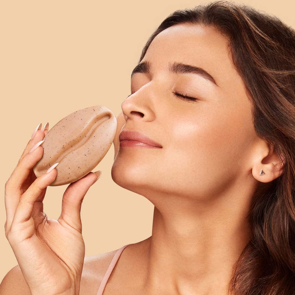 Woman applying a beige cosmetic product to her face against a beige background