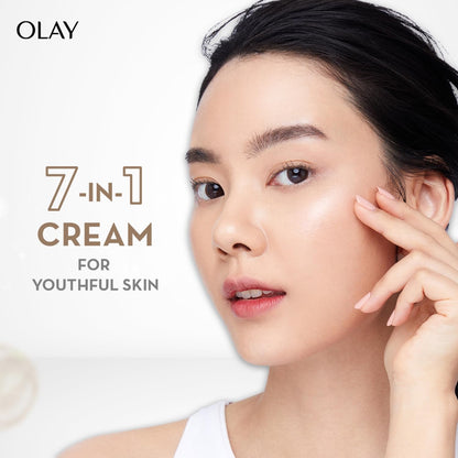 Woman applying Olay 7-in-1 cream to her face with a white background