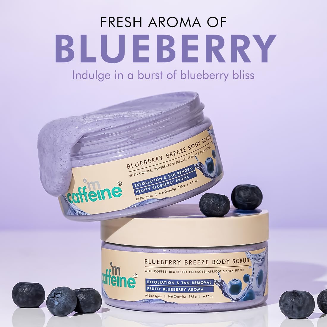 Two jars of 'm caffeine Blueberry Breeze Body Scrub' with blueberries on a light purple background.