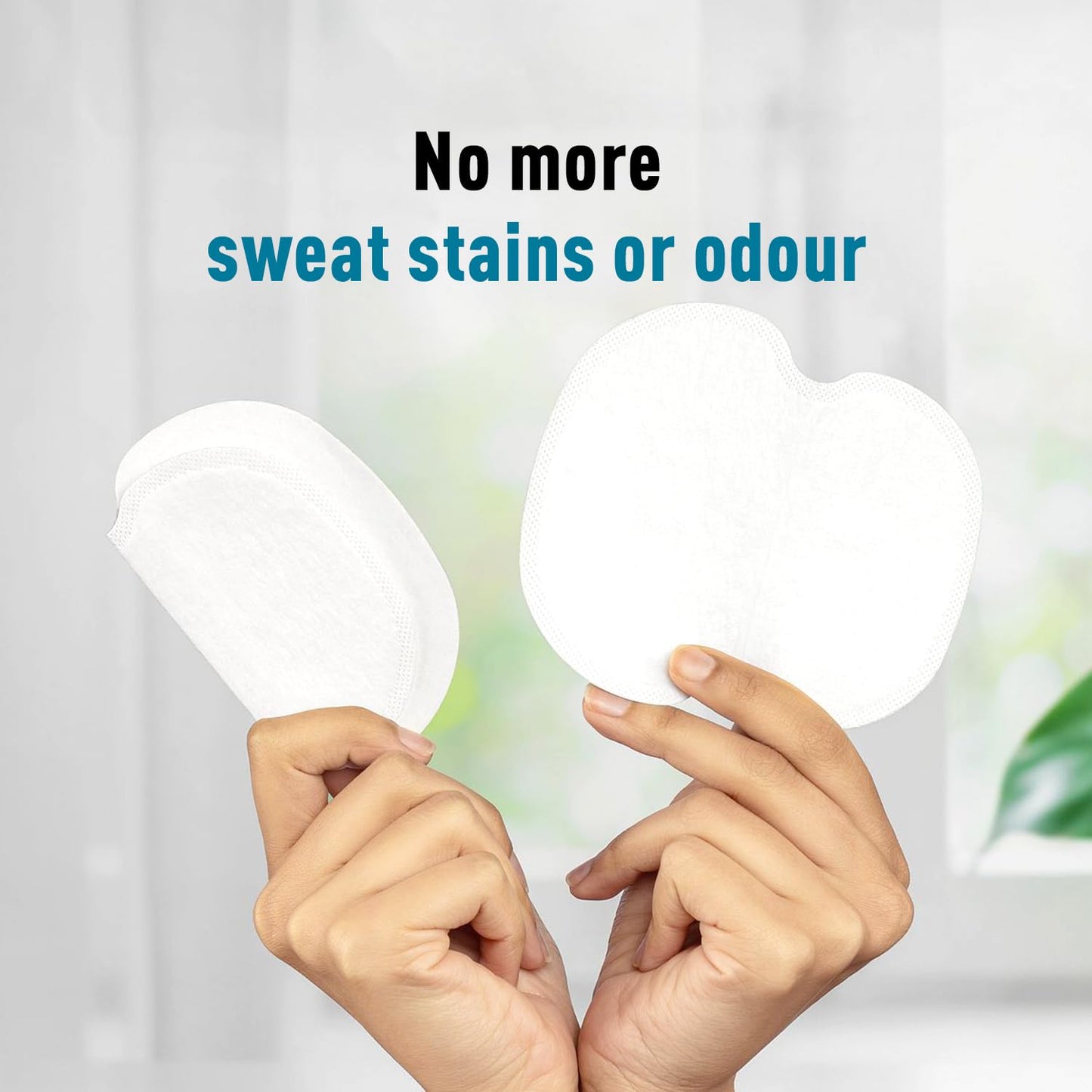 Two hands holding white sweat pads with text 'No more sweat stains or odour' on a blurred background.