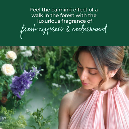 Woman in a pink dress standing in a forest with text about cypress and cedarwood fragrance.