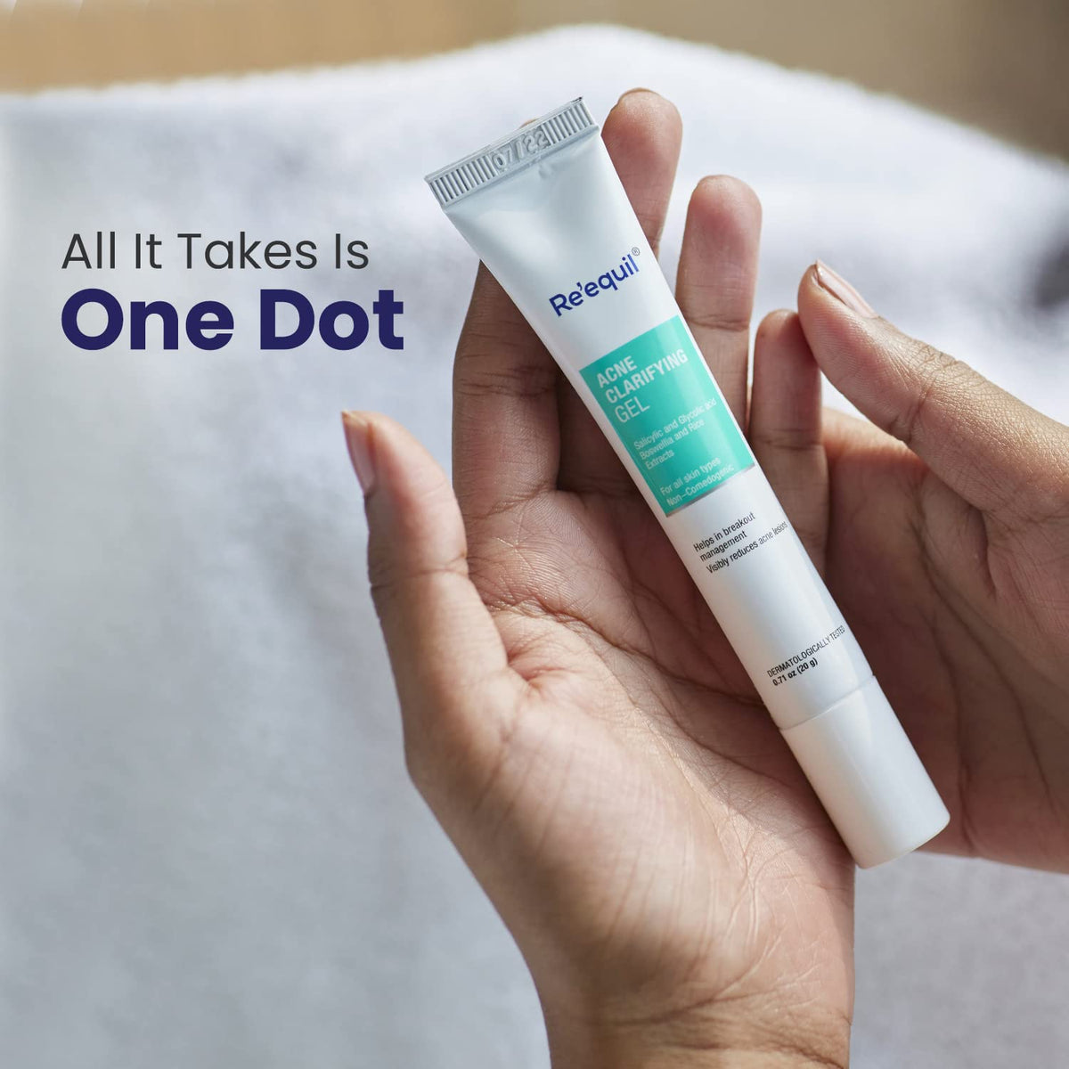 Hand holding a tube of Requell acne treatment gel with text 'All It Takes Is One Dot' on a blurred background