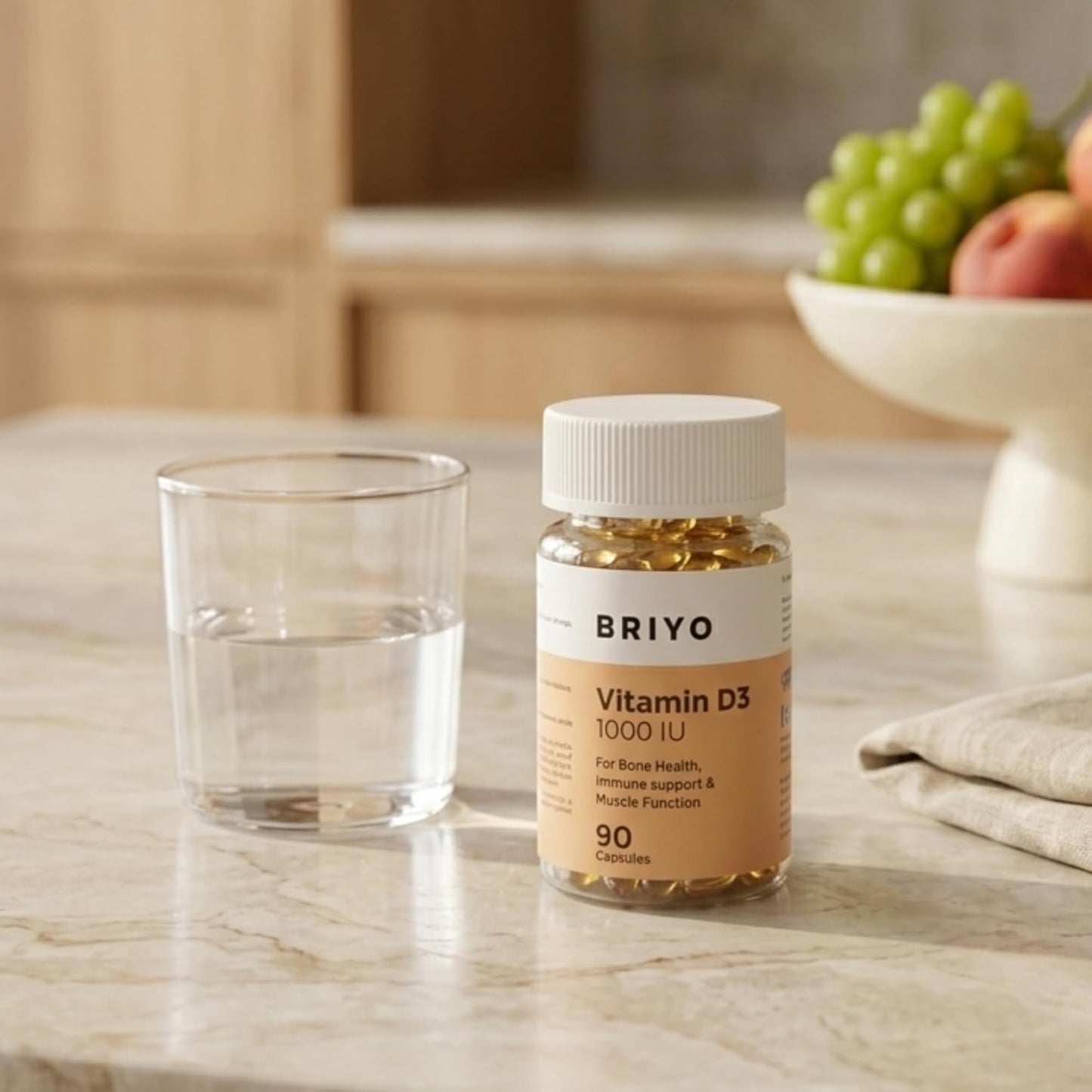 Briyo Vitamin D3 supplement bottle on a marble surface with a glass of water and fruit in the background.