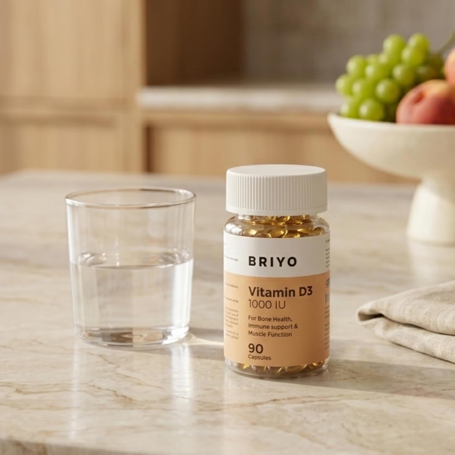 Briyo Vitamin D3 supplement bottle on a marble surface with a glass of water and fruit in the background.