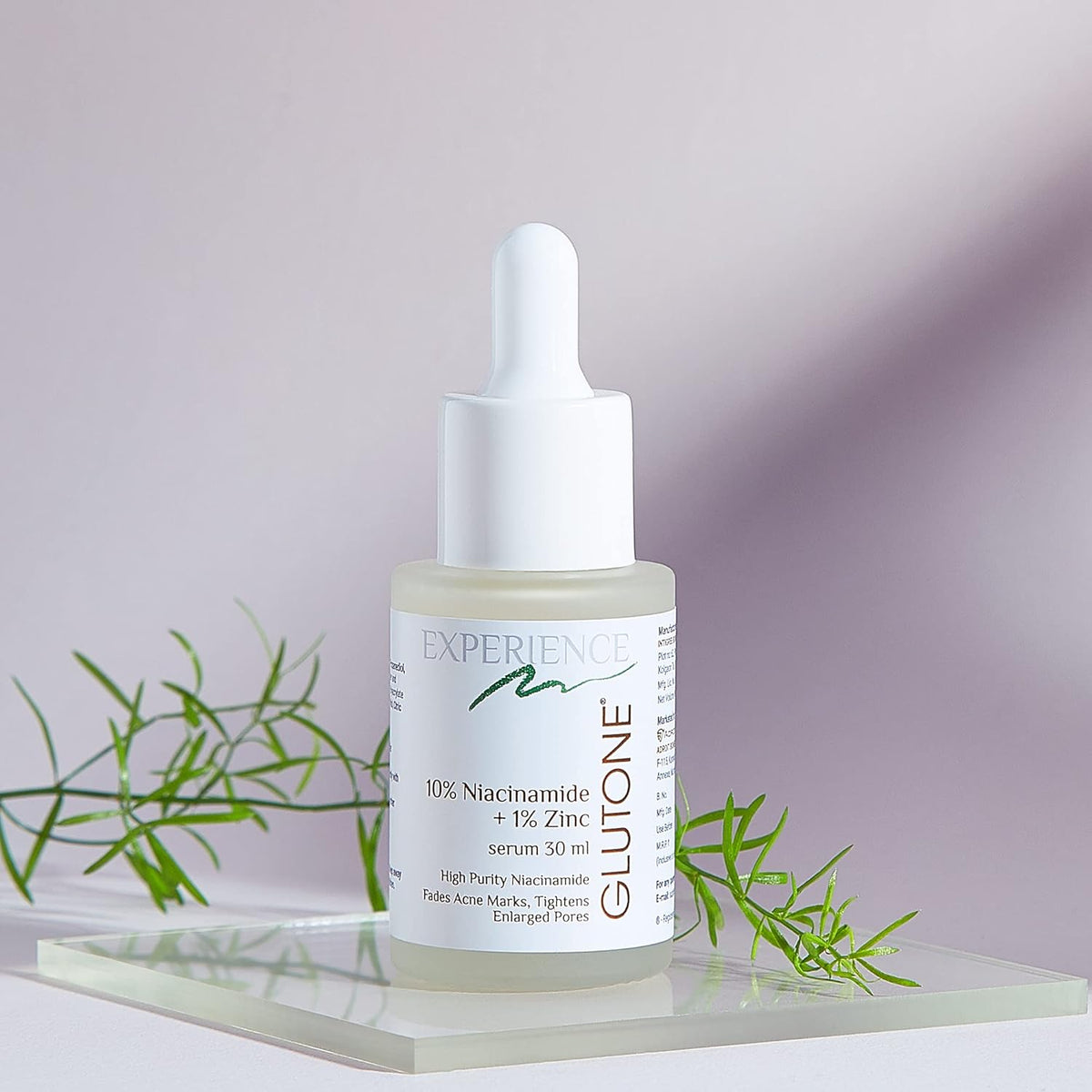 Skincare serum bottle with dropper on a light surface with green leaves in the background