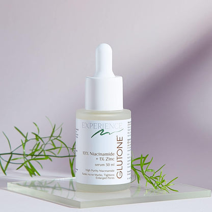 Skincare serum bottle with dropper on a light surface with green leaves in the background