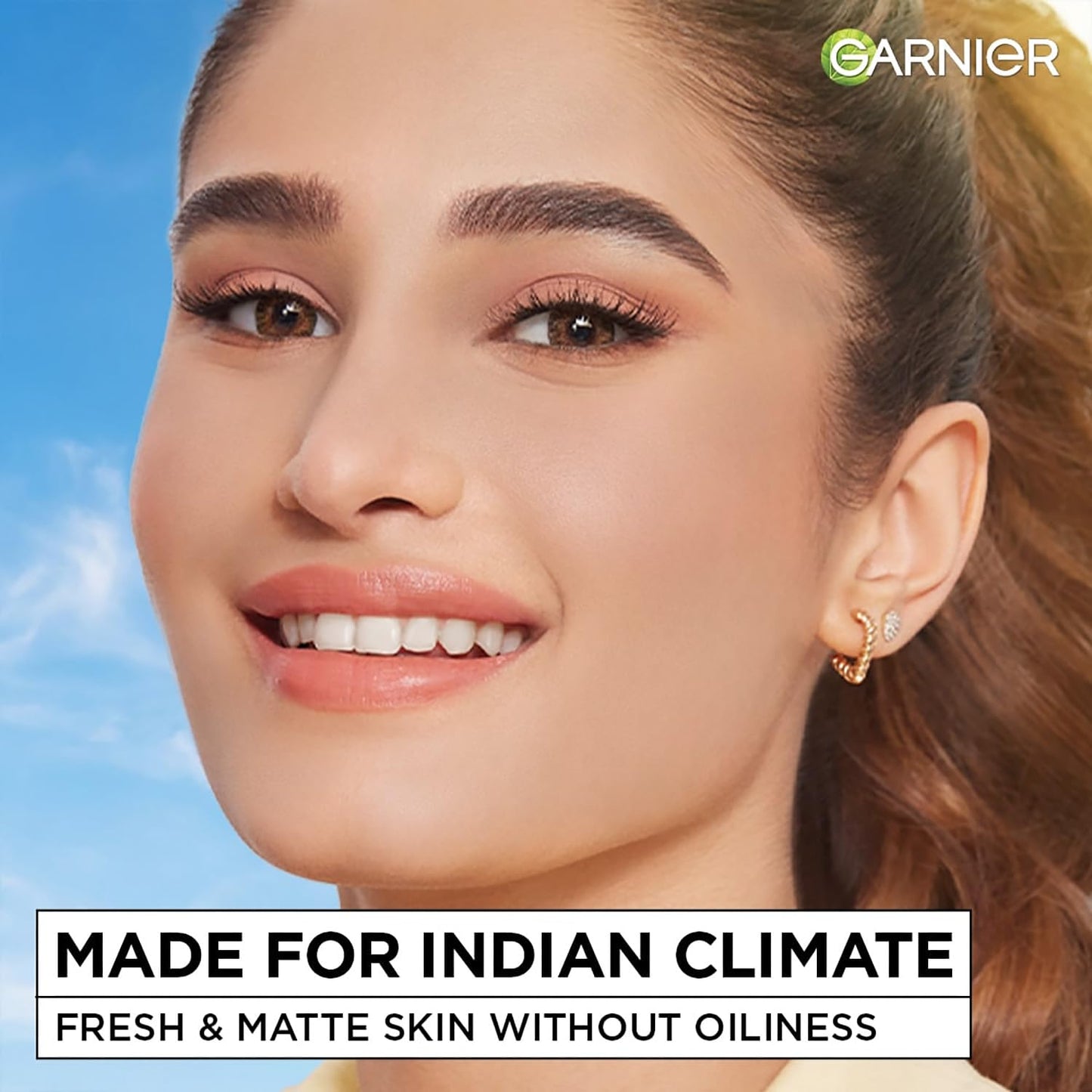 Woman with makeup and earrings against a blue sky, with Garnier branding and text about skin care.