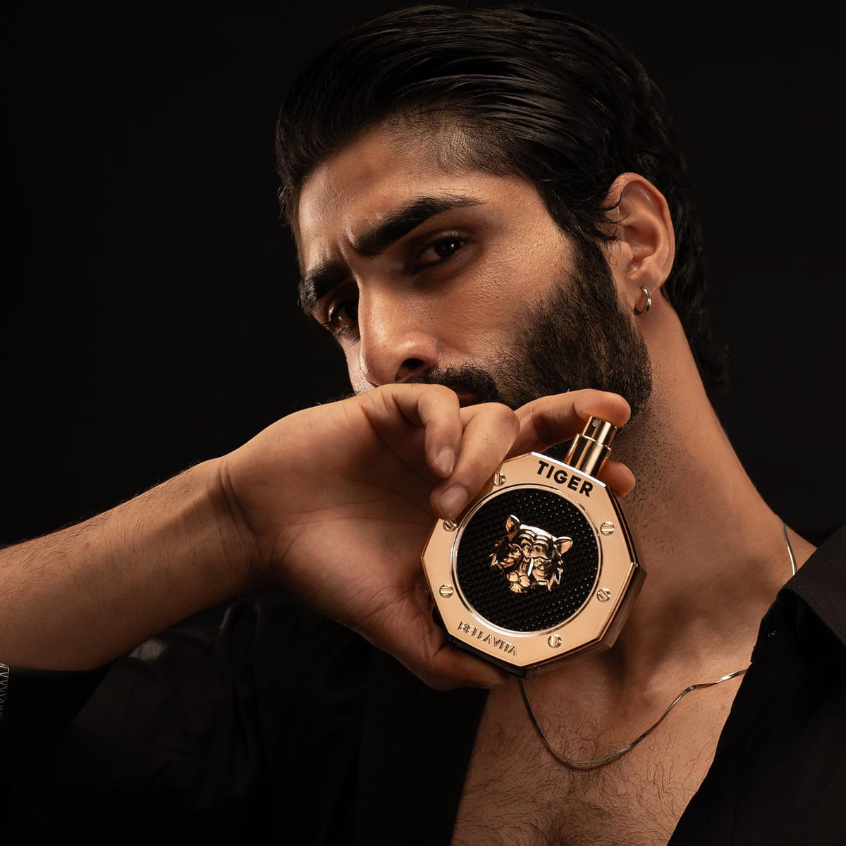 Man holding a gold and black tiger-themed perfume bottle against a dark background