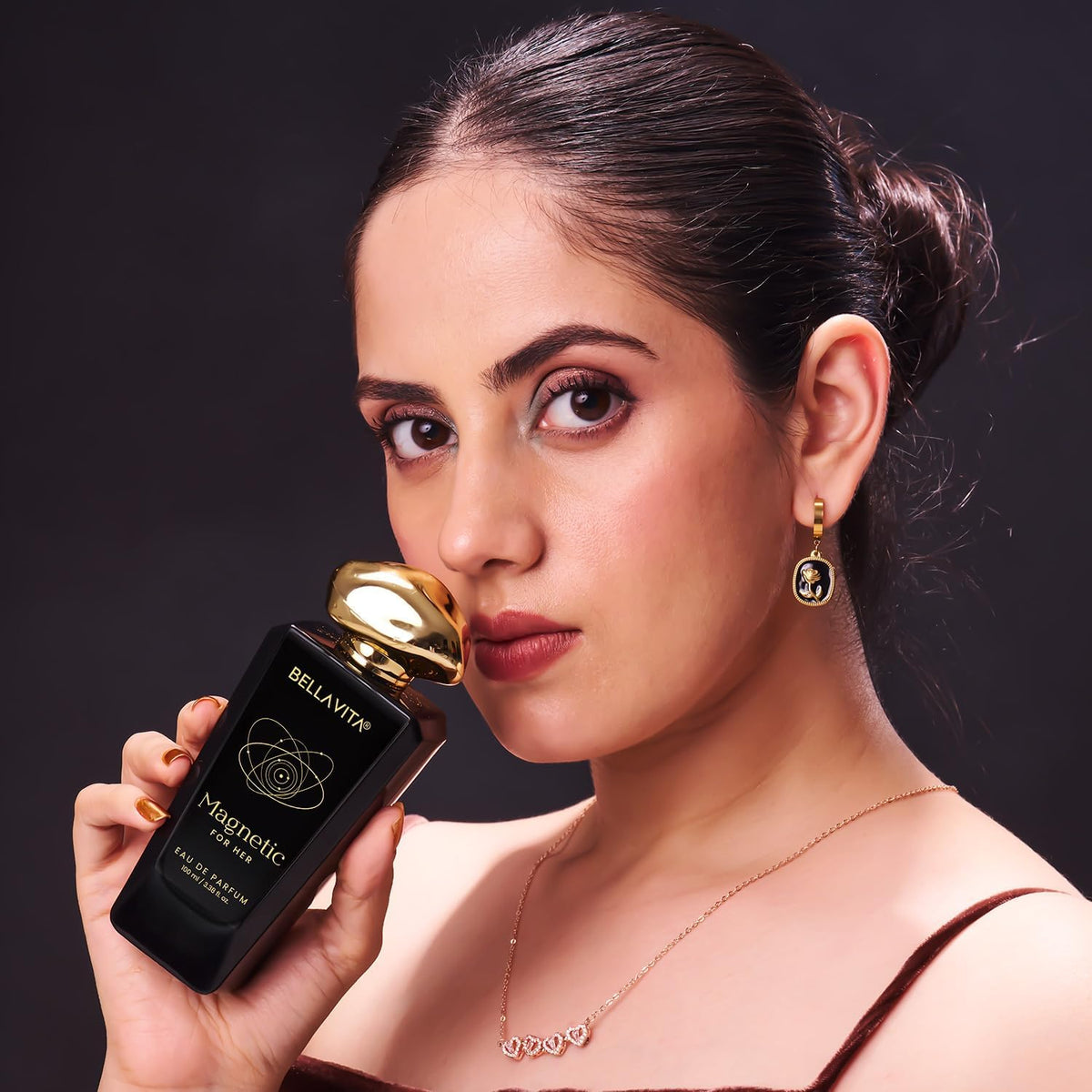 Woman holding a black and gold perfume bottle with a dark background