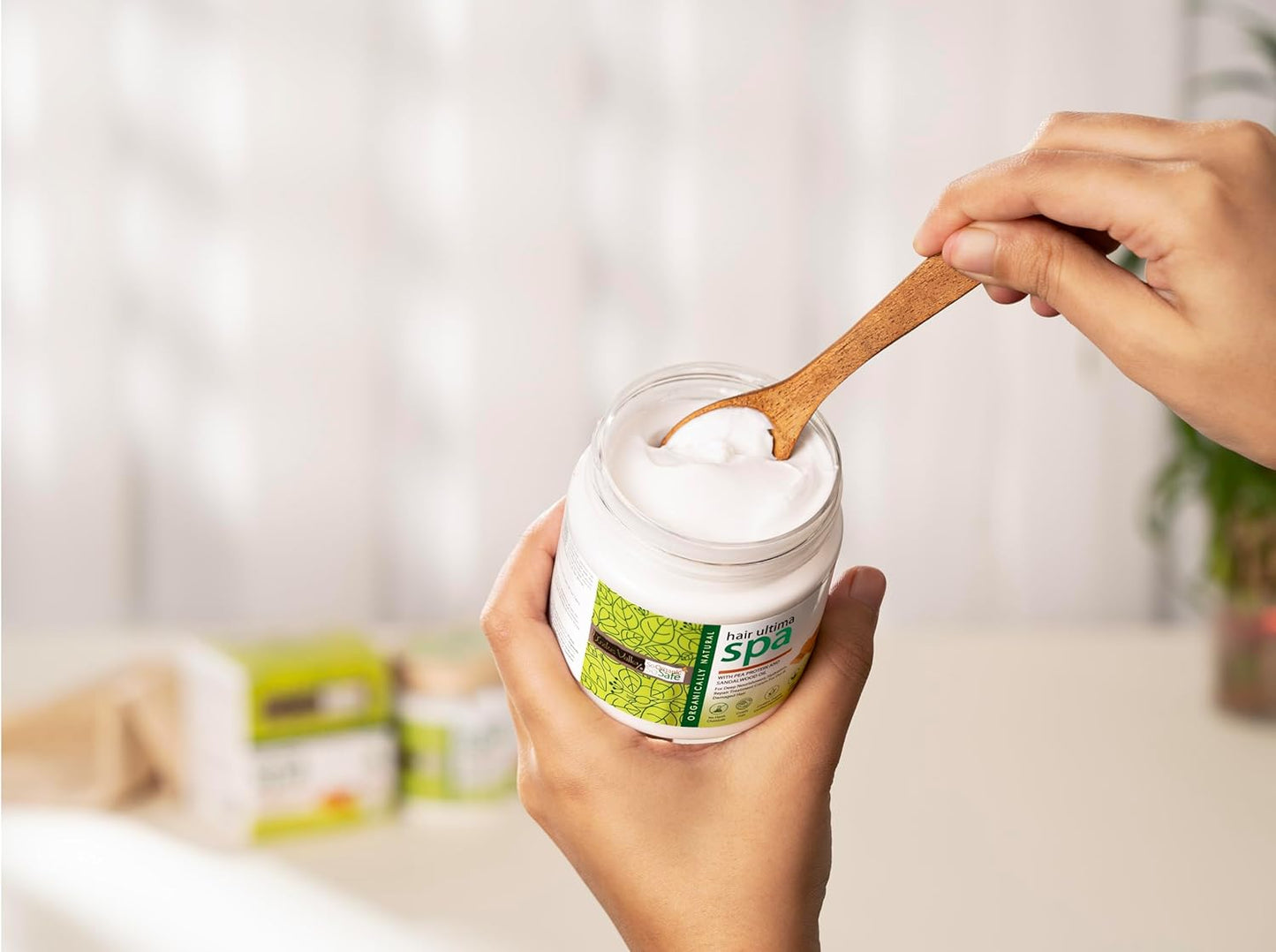 Person holding a jar of white powder with a wooden spoon, blurred background