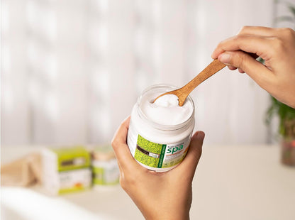 Person holding a jar of white powder with a wooden spoon, blurred background