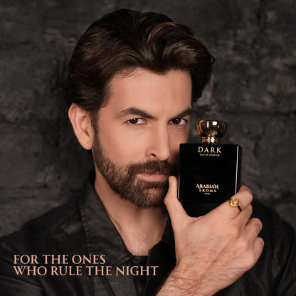 Man holding a black Arabian Aroma Dark perfume bottle against a dark background