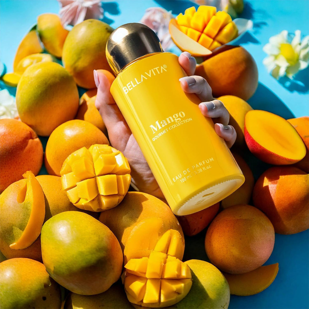 Hand holding a yellow Bellavita Mango perfume bottle surrounded by mangoes on a blue background