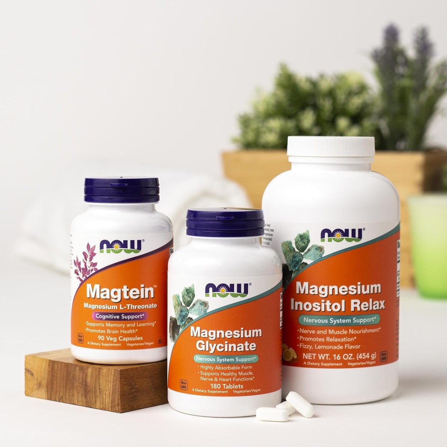Three NOW Supplements bottles on a white surface with a blurred plant background