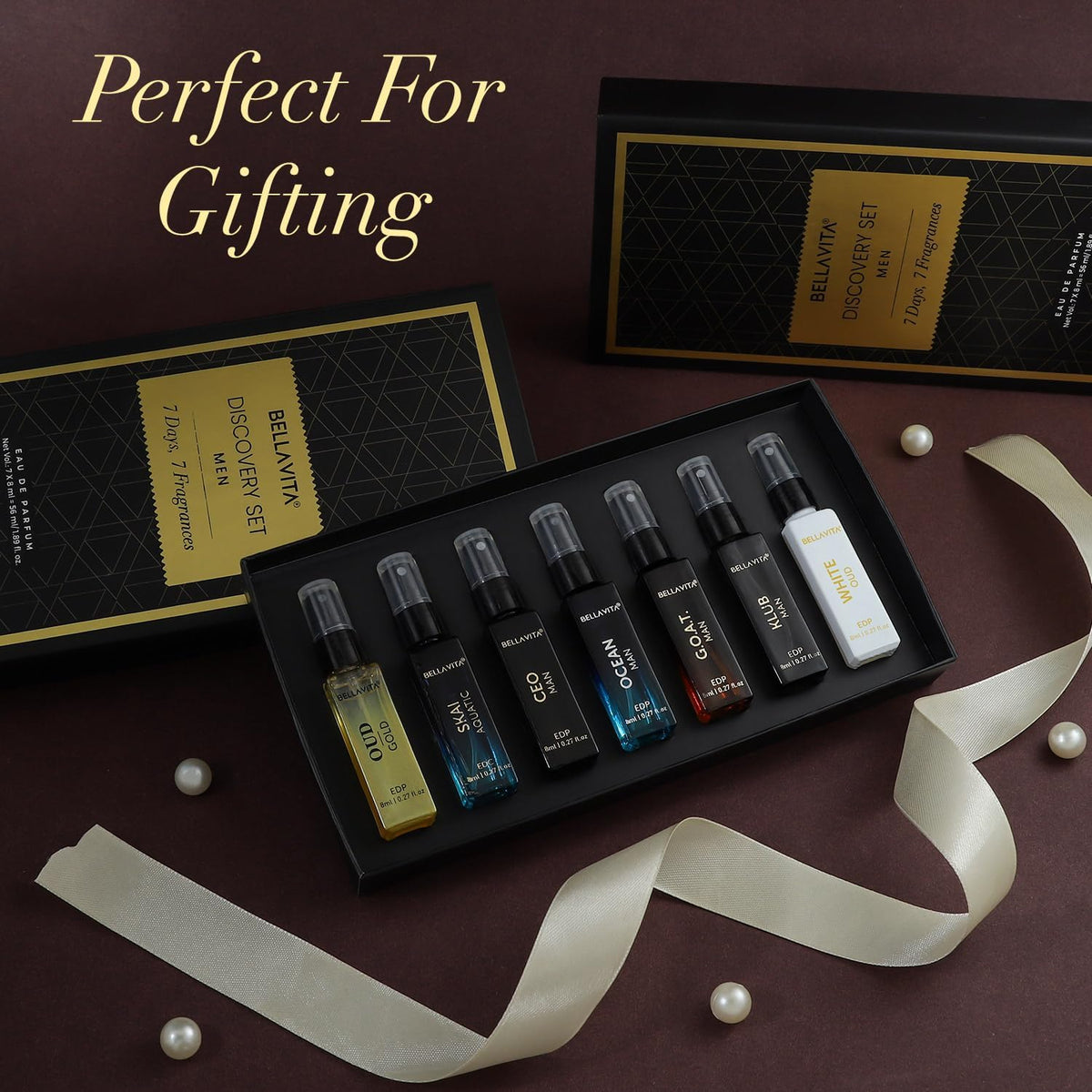 Set of small perfume bottles in a black box with decorative ribbons and pearls on a dark background.