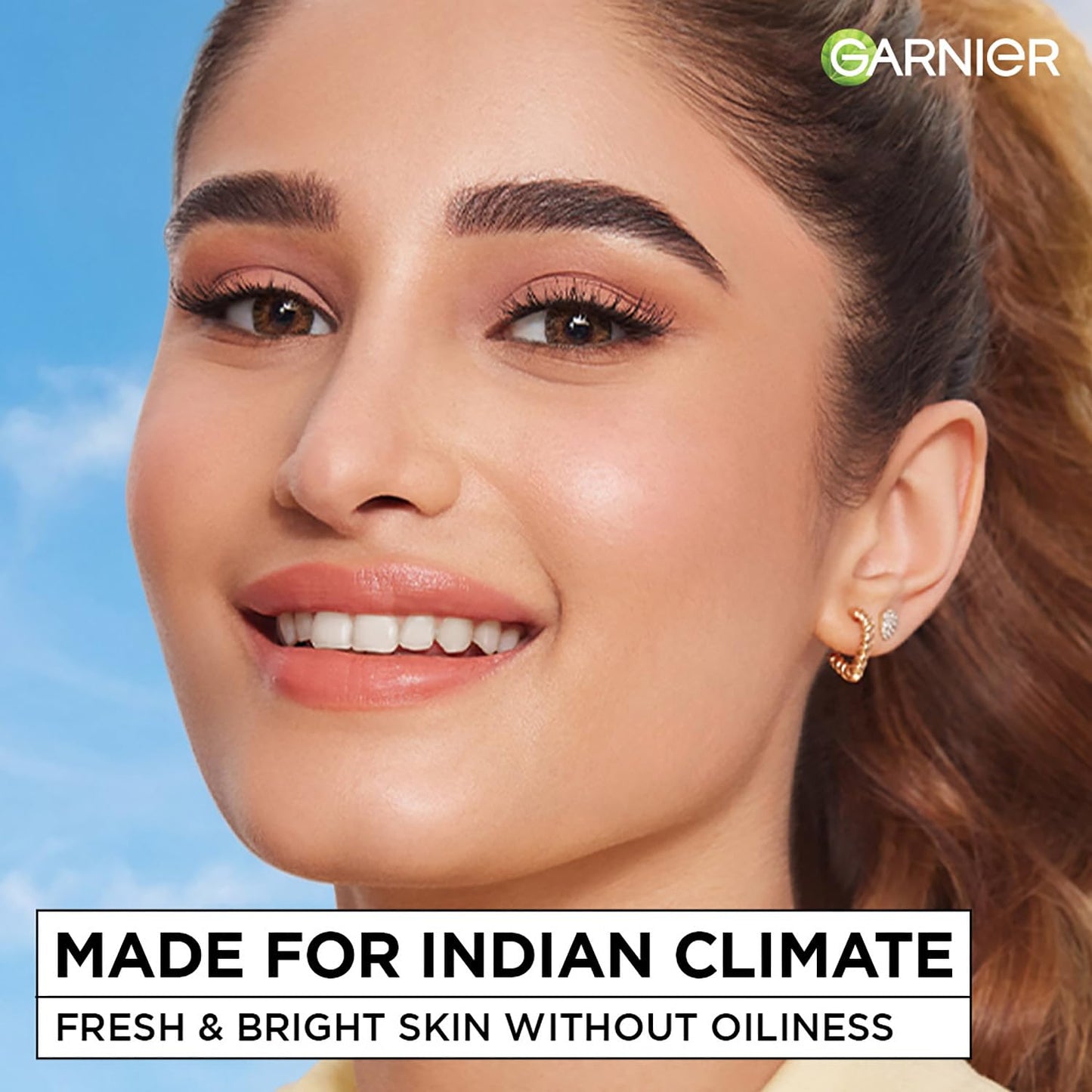 Woman with a clear complexion against a blue sky, promoting Garnier's skincare product.