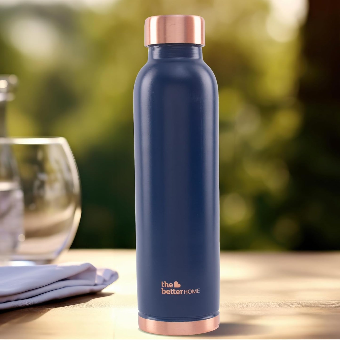 Blue water bottle with rose gold cap on a wooden table outdoors