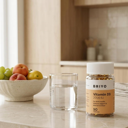 Briyo Vitamin D3 bottle on a kitchen counter with a glass of water and fruit bowl.