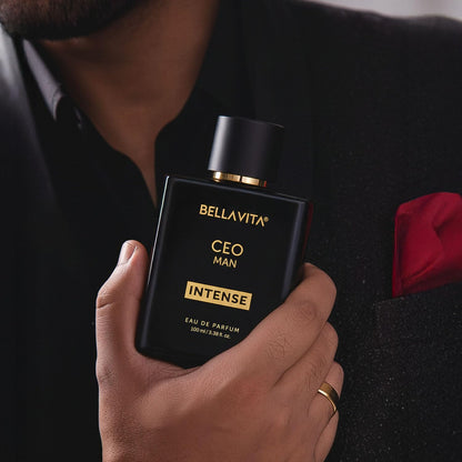 Hand holding a black Bellavita perfume bottle labeled 'CEO MAN Intense' against a dark background.
