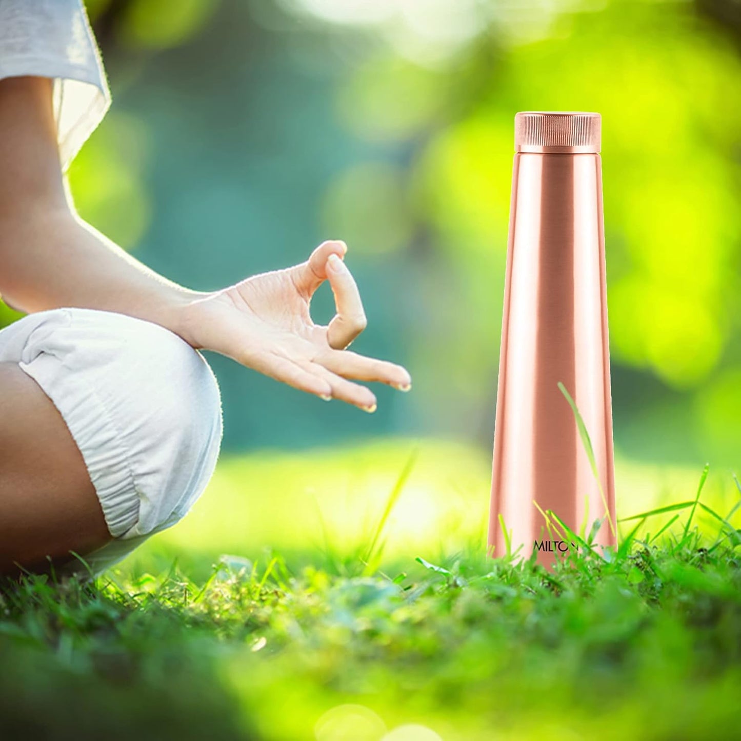 Person meditating on grass with a rose gold bottle in the foreground