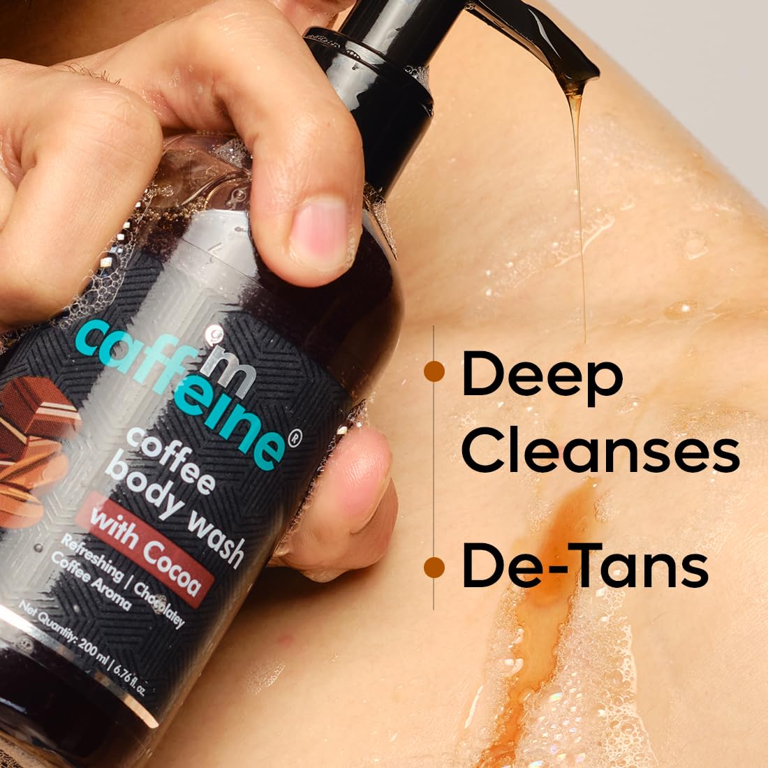 Hand using caffeine coffee body wash with cocoa on skin, labeled 'Deep Cleanses' and 'De-Tans'.