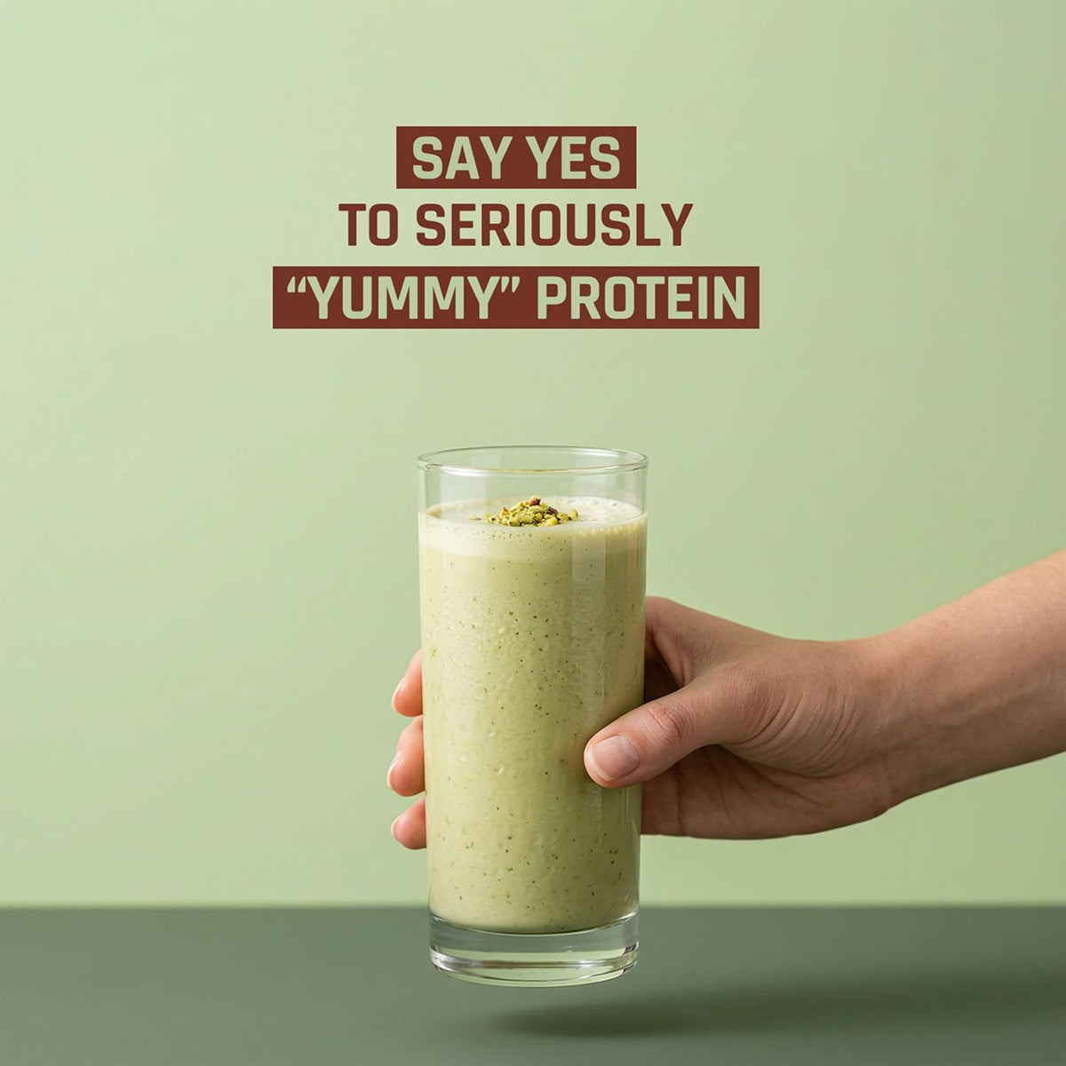 Hand holding a glass of protein shake with promotional text on a green background