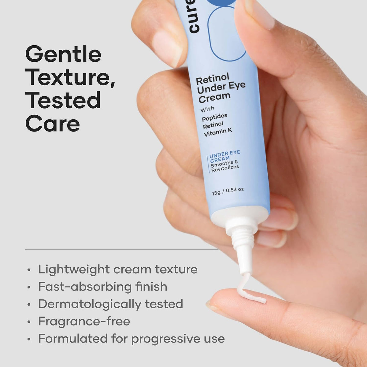 Hand holding a tube of Cure Retinol Under Eye Cream with product details on a gray background