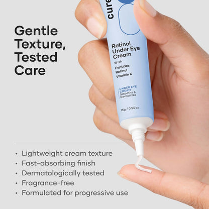 Hand holding a tube of Cure Retinol Under Eye Cream with product details on a gray background